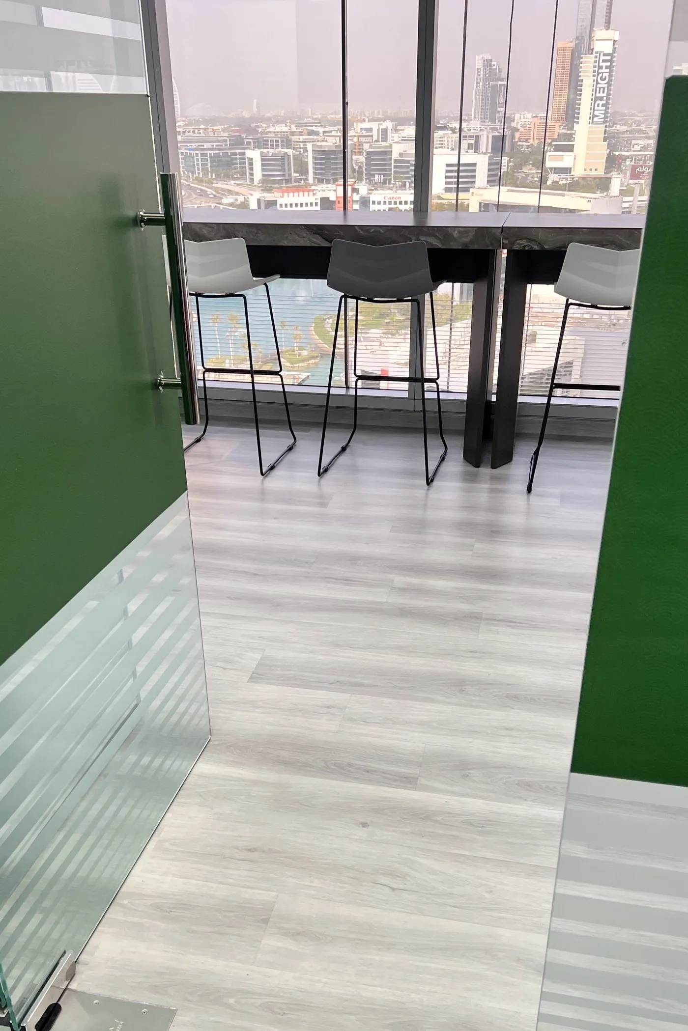 Breakout room behind green glazed partitions, with a bar table and stools at the window